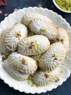 powdered pastries on a white plate next to bowls of green and pink sprinkles