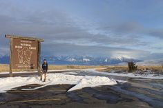 a woman standing in front of a sign on the side of a road covered in snow