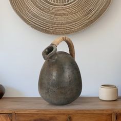 a large gray vase sitting on top of a wooden table next to a wall hanging