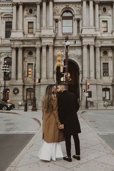 a man and woman standing in front of an old building with traffic lights on the street