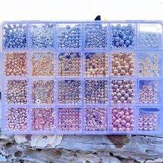 a plastic container filled with lots of different types of bead beads on top of a piece of wood