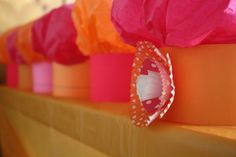 several orange and pink vases are lined up on the shelf with paper flowers in them