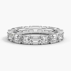 a white gold ring with baguetts and diamonds on the sides, set against a plain background