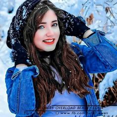 a woman wearing a blue jacket in the snow with her hands on her head and looking at the camera