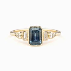 One of a kind ring In stock ready to ship in size 7 1.03ct Deep Teal Blue Montana Sapphire, 6.52x4.56x3.23mm, si1, Heated 0.71ct Light Blue Montana Sapphire, 6.44x4.39x2.46mm, vs1 clarity, Heated Bandwidth: approx. 1.5mm Accent diamond 0.19ctw Low profile bezel setting Ethically sourced solid 14k yellow gold and gemstones Packaged in a recyclable kraft ivory ring box Unique Sapphire Rings, Rings 2023, Colored Stone Engagement Rings, Ivory Ring, Ring Inspo, Ring Emerald Cut, Bezel Engagement Ring, Blue Diamond Ring, Dainty Gold Rings