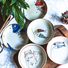 four hand painted plates with fish on them and a plant in the middle, sitting on a marble countertop