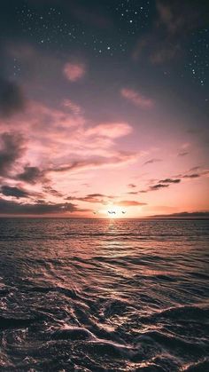 the sun is setting over the ocean with waves in front of it and stars in the sky