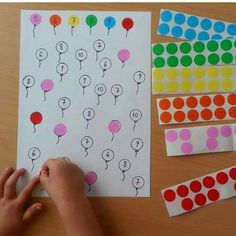 a child's hand is on the paper next to some dots and balloons