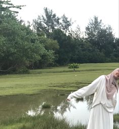 a woman standing in front of a body of water wearing a white dress and head scarf