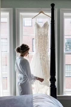 a woman standing in front of a window next to a wedding dress