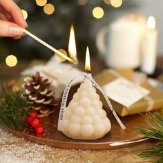 someone lighting a candle on top of a wooden plate with pine cones and other decorations