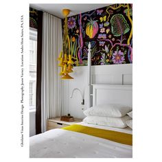 a white bed sitting next to a window with colorful wallpaper on the walls behind it