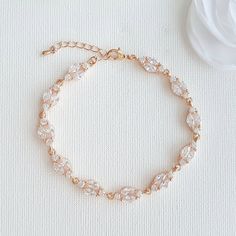 a gold bracelet with crystal beads and a white flower on top of a white surface