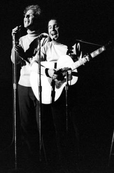 two men standing next to each other holding guitars and singing into microphones on stage