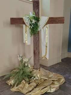 a wooden cross with flowers and greenery on the ground next to it in front of a wall