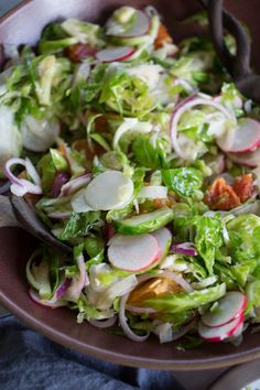 a salad with lettuce, radishes and onions in a brown bowl