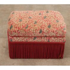 a red and beige ottoman with fringes on the bottom, sitting on a tile floor