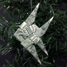 an ornament made out of dollar bills hanging from a christmas tree with green needles