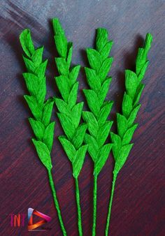 three green plants are sitting on a wooden table, one is made out of paper and the other has leaves