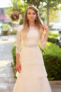 a woman in a white dress is standing on the sidewalk with her hair blowing in the wind