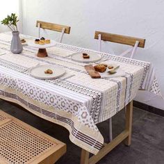 a table with plates and cups on it in front of a white wall next to a bench