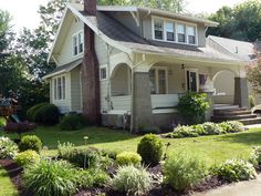 a house that is in the middle of some bushes and flowers on the front lawn