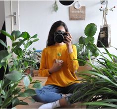 a woman sitting on the floor taking a selfie in front of potted plants