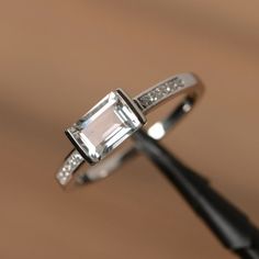 It is a natural white topaz ring. The main stone is 5mm*7mm emerald cut.The basic metal is sterling silver and plated with rhodium.To change the metal to a solid gold (white/rose) or platinum is also available, please ask for a quotation if you want.You can also go to my shop Home for more elegant rings: https://www.etsy.com/shop/godjewelry?ref=hdr_shop_menuTopaz is November birthstone.More topaz rings:https://www.etsy.com/shop/godjewelry?ref=hdr_shop_menu&section_id=20715039Customization is White Emerald Cut Cubic Zirconia Ring, White Solitaire Emerald Cut Jewelry, White Emerald Cut Solitaire Jewelry, Timeless Emerald Cut Topaz Ring With Prong Setting, Silver 14k White Gold Diamond Ring, Emerald Cut, Classic Emerald-cut Topaz Ring In Sterling Silver, Timeless Emerald-cut Topaz Ring With Prong Setting, Elegant Rectangular Topaz Promise Ring, Elegant Octagon Topaz Promise Ring