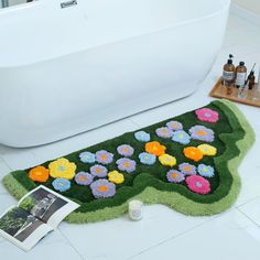 a bath mat with flowers on it next to a white tub and other bathroom items