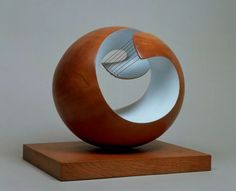 a wooden sculpture sitting on top of a wooden block with a metal object in it's center