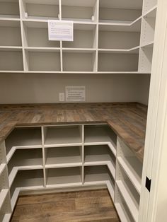 an empty closet with white shelving and wood flooring