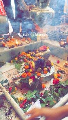 a person is lighting candles in front of a shrine with flowers and leaves on the ground