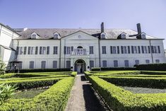 a large white building with hedges in front of it and a walkway leading to the entrance