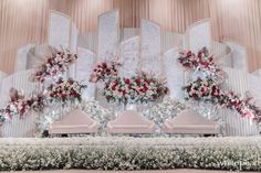 an elaborately decorated stage with floral arrangements and chairs in front of the stage wall