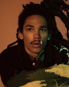 a man with dreadlocks wearing a tie and looking at the camera while sitting down