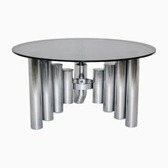 a glass table with silver metal legs and four cylinders on each end, in front of a white background