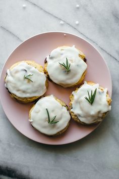 three small pastries on a pink plate with white icing and green sprigs