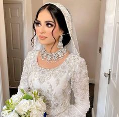 a woman in a wedding dress holding a bouquet and wearing a necklace with pearls on it