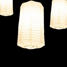 three white lanterns hanging from the ceiling in front of a black background with one light turned on