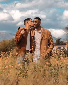 two men standing in tall grass kissing each other