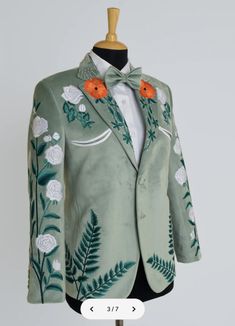 a green suit with white flowers and leaves on the lapel has an orange bow tie