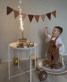 a little boy standing in front of a table with a birthday cake on top of it