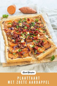 a square pizza with onions, tomatoes and herbs on it sitting on a wooden cutting board