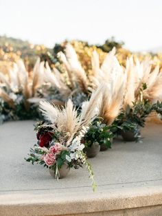 an arrangement of flowers and plants are on the concrete table outside in front of some bushes