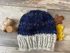 a blue and white knitted hat next to some autumn leaves on a wooden surface