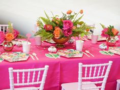 the table is set with pink and orange flowers in vases, plates and napkins