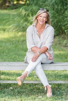 a woman is sitting on a bench in the grass and smiling at the camera with her legs crossed