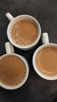 three white cups filled with liquid on top of a table