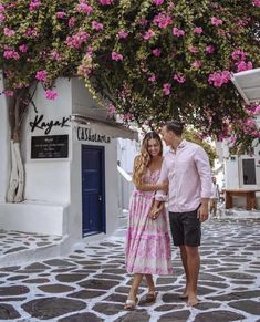 a man and woman standing in front of a building with pink flowers on the tree