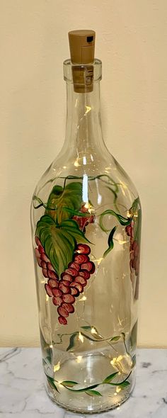 a glass bottle with grapes painted on the side and lights in the bottom, sitting on a marble surface